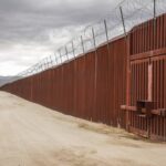 A formidable border wall, topped with barbed wire, symbolizes the geopolitical and security challenges facing regions affected by drug trafficking and cross-border violence.