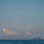 Cargo vessels navigate the open sea under a calm sky, symbolizing global trade amid geopolitical tensions.