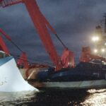 A damaged vessel, the 'Uglad', is being lifted by a crane at night, highlighting a maritime incident that may be linked to the shadowy operation involving beetles and candy shipments that allegedly aided Russian troops.